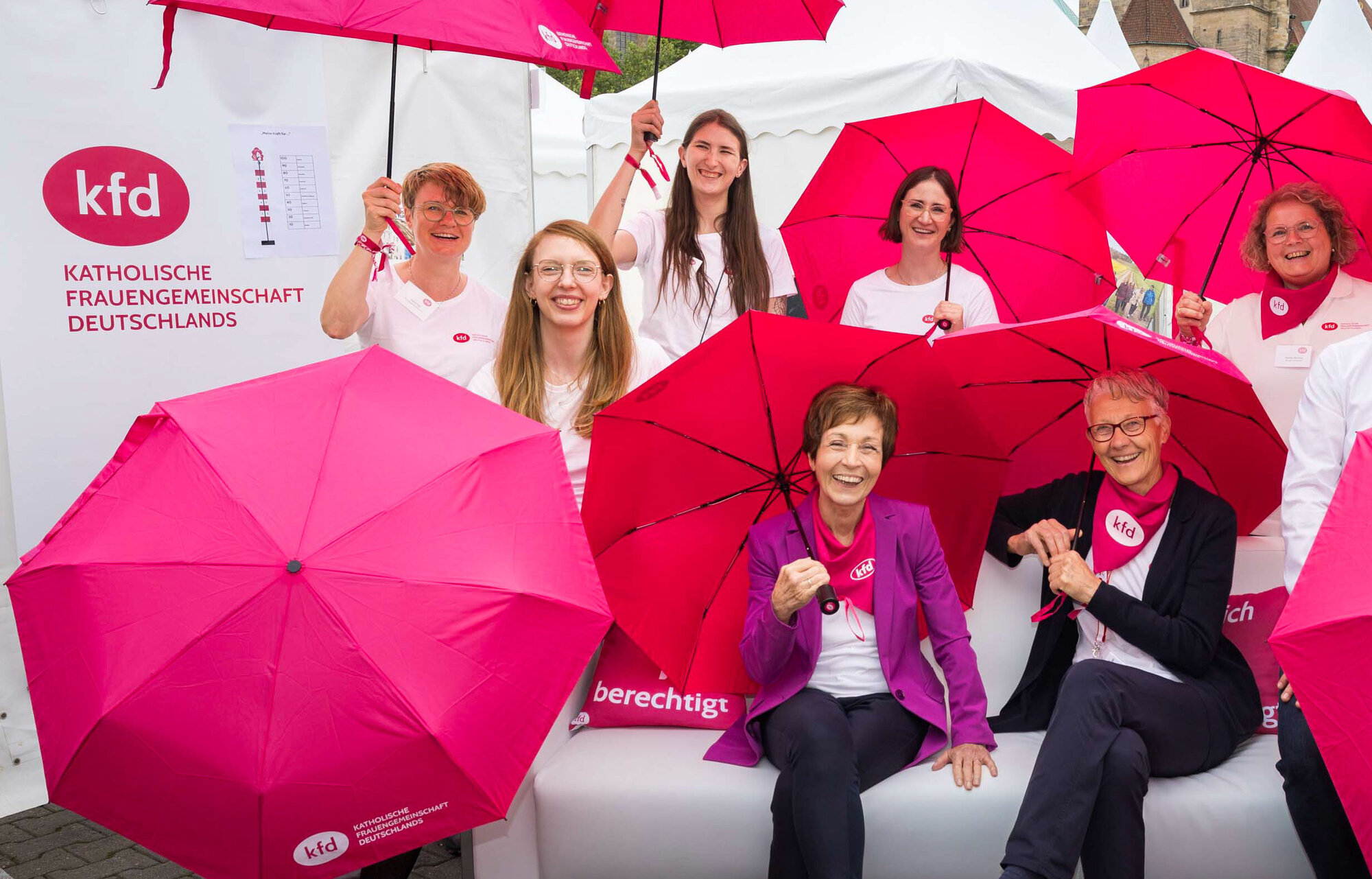 Frauen auf einem Sofa halten purpurfarbene Schirme hoch